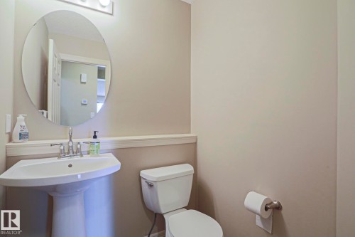 Bathroom featuring a pedestal sink with chrome faucet, an oval mirror, and a wall-mounted light fixture - 6215 60 Street, Beaumont, AB - Indoor Photo Showing Bathroom
