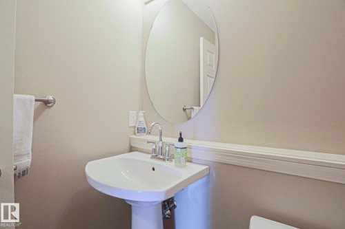 Pedestal sink with chrome faucet, circular mirror, and neutral wall tones - 6215 60 Street, Beaumont, AB - Indoor Photo Showing Bathroom
