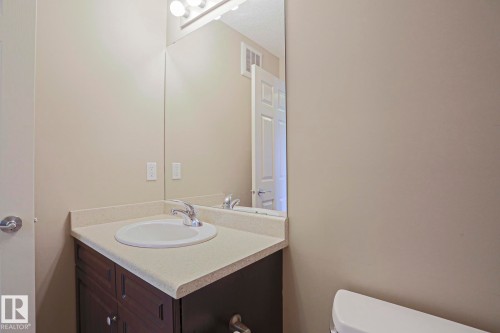 Bathroom vanity featuring a dark wood-finish cabinet with storage, a speckled countertop, and an integrated white basin - 6215 60 Street, Beaumont, AB - Indoor Photo Showing Bathroom