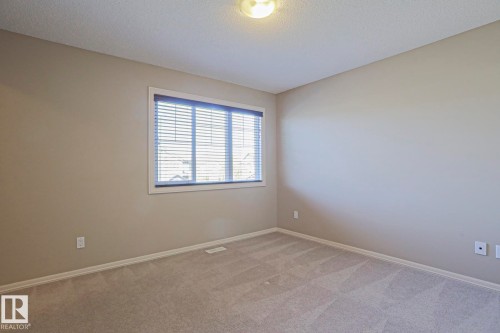 Carpeted room with neutral walls, a window featuring horizontal blinds, white baseboards, and a ceiling-mounted light fixture - 6215 60 Street, Beaumont, AB - Indoor Photo Showing Other Room