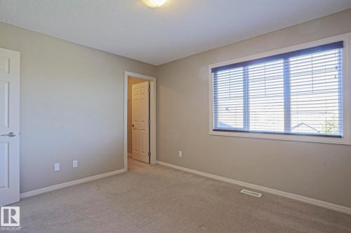 Room featuring a large window with horizontal blinds, neutral-toned walls, plush carpeting, and white trim - 6215 60 Street, Beaumont, AB - Indoor