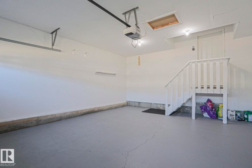 Spacious garage featuring a durable gray floor, white painted walls, internal staircase access, and an automatic garage door opener - 6215 60 Street, Beaumont, AB - Indoor