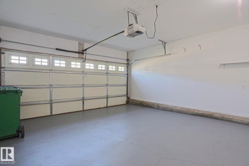 Spacious garage featuring a sectional overhead door with window inserts, an automatic garage door opener, painted concrete flooring, and white walls - 6215 60 Street, Beaumont, AB - Indoor Photo Showing Garage