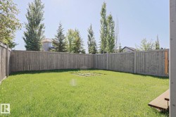 Expansive backyard featuring a green lawn, full privacy fencing, and a central stone paver area - 