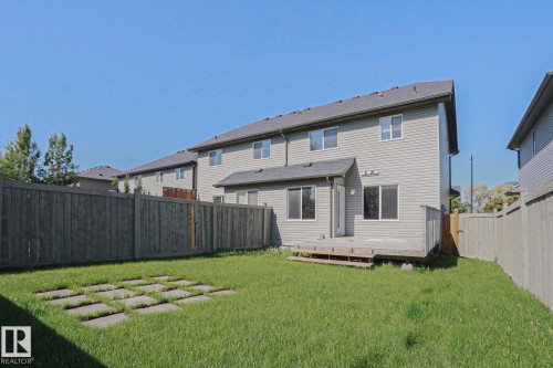 Fenced backyard featuring a wood deck, stone pavers, and a two-story exterior with horizontal siding and multiple windows - 6215 60 Street, Beaumont, AB - Outdoor With Exterior