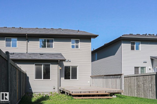 Rear exterior featuring light grey siding, dark shingle roofing, and a ground-level wood deck - 6215 60 Street, Beaumont, AB - Outdoor With Exterior