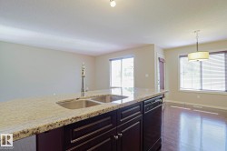 Kitchen island featuring a double basin sink, chrome pull-down faucet, and light-toned speckled countertop - 