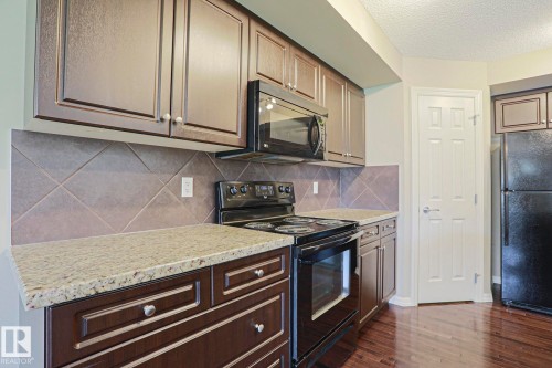 Kitchen featuring dark wood cabinetry, light speckled countertops, a tile backsplash, and black appliances including an electric range and microwave - 6215 60 Street, Beaumont, AB - Indoor Photo Showing Kitchen