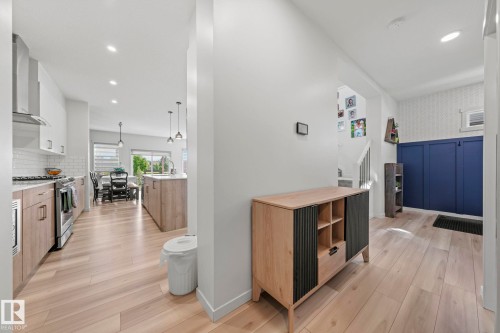 Open-concept living space featuring wood-finish flooring, recessed lighting, a modern kitchen with a stainless steel range hood, white subway tile backsplash, and a blue accent wall - 1931 Westerra Lane, Stony Plain, AB 