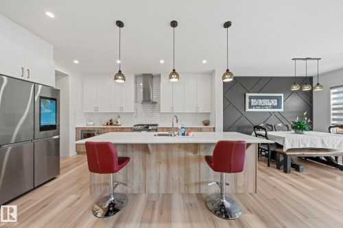 Spacious kitchen featuring a large central island with seating, stainless steel appliances, a white subway tile backsplash, and light wood-finish flooring - 1931 Westerra Lane, Stony Plain, AB 