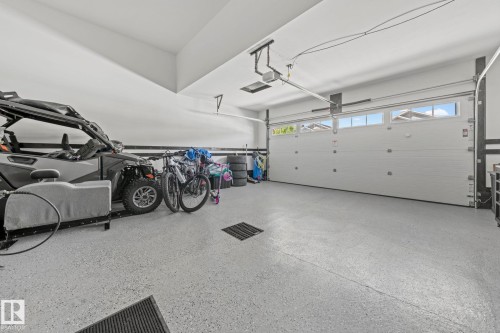 Spacious garage featuring a light-colored epoxy floor, white paneled garage door with upper-level windows, and overhead lighting - 1931 Westerra Lane, Stony Plain, AB 