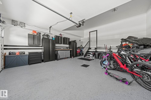 Spacious garage featuring a durable epoxy floor coating, built-in storage cabinets, a dedicated workbench area, interior access via stairs, and an automatic garage door opener - 1931 Westerra Lane, Stony Plain, AB 