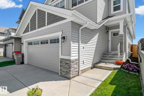 Contemporary exterior featuring light gray horizontal siding, an attached garage with overhead panel door and transom windows, a covered front entry with stone veneer accents, and a concrete driveway - 1931 Westerra Lane, Stony Plain, AB 