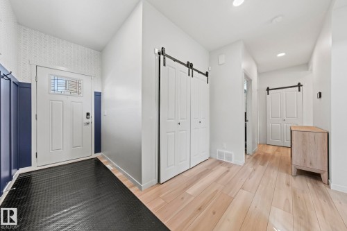Entryway featuring light wood-finish flooring, white paneled doors, and two sets of white barn doors with black hardware - 1931 Westerra Lane, Stony Plain, AB 