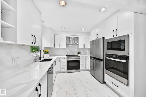 Contemporary kitchen featuring white cabinetry, integrated stainless steel appliances, marble-look countertops, a black undermount sink with a matching faucet, and recessed lighting - 10323 138 Street, Edmonton, AB 
