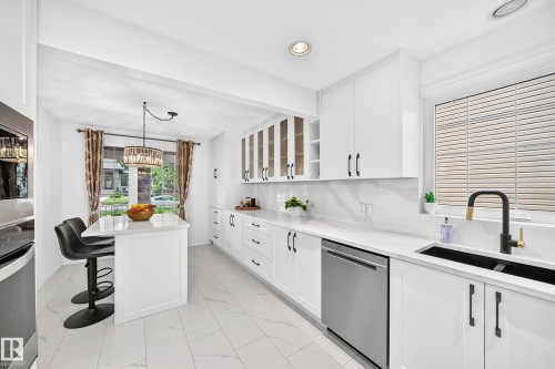 Contemporary kitchen featuring white cabinetry with black hardware, stainless steel dishwasher, black double basin sink with matte black faucet, and white countertops with a matching backsplash - 10323 138 Street, Edmonton, AB 