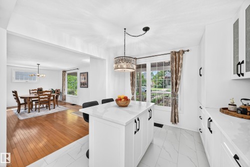 Kitchen featuring a central island with white countertop, white cabinetry with black hardware, and marble-look floor tiles - 10323 138 Street, Edmonton, AB 