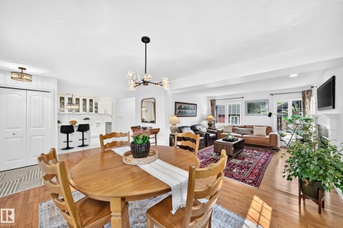 Open-concept living area featuring wood-finish flooring, a contemporary chandelier, a white fireplace mantel, and recessed lighting - 10323 138 Street, Edmonton, AB 