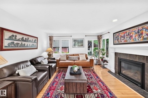 Living area featuring light wood-finish flooring, a contemporary fireplace with a dark tile surround and white mantel, recessed lighting, and multiple windows with white trim - 10323 138 Street, Edmonton, AB 