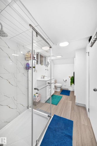 Contemporary bathroom with a glass-enclosed shower featuring marble-look tile, wood-finish flooring, and recessed lighting - 10323 138 Street, Edmonton, AB 