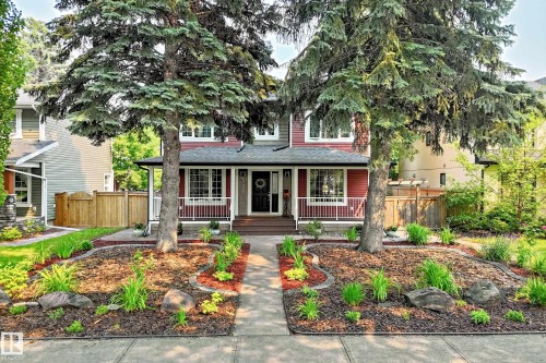 Two-story residence featuring a covered front porch with white railings, a dark wood-finish front door, and a concrete pathway - 10323 138 Street, Edmonton, AB 