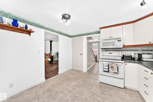 Kitchen featuring white cabinetry with wood-finish trim, white appliances including a built-in microwave and electric range, and a light-toned patterned floor - 191 Ridgewood Terrace, St. Albert, AB 