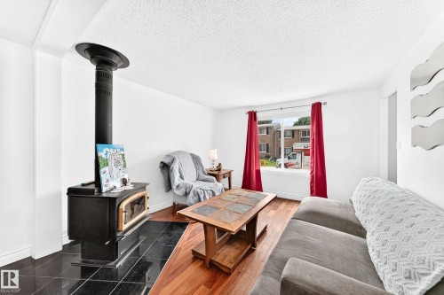 Living area featuring a black wood-burning stove with a tiled base, hard-surface flooring, and a window with natural light - 191 Ridgewood Terrace, St. Albert, AB 