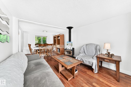 Open-concept living area featuring rich wood-finish flooring, a freestanding wood-burning stove, and a dining space with a window overlooking exterior greenery - 191 Ridgewood Terrace, St. Albert, AB 