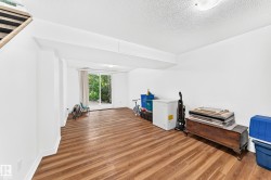 Spacious lower-level room featuring wood-finish flooring, white walls, and a sliding glass door - 