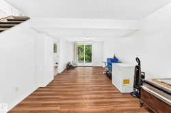 Spacious lower level featuring wood-finish flooring, white painted walls, and a sliding glass door leading to outdoor greenery - 