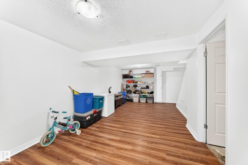 Finished basement space featuring wood-finish flooring, recessed ceiling lighting, built-in shelving, white baseboards, and a paneled interior door - 191 Ridgewood Terrace, St. Albert, AB 