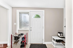 Entryway featuring a white paneled door with an arched glass insert, a privacy glass sidelight, light neutral wall paint, and light wood-finish flooring - 