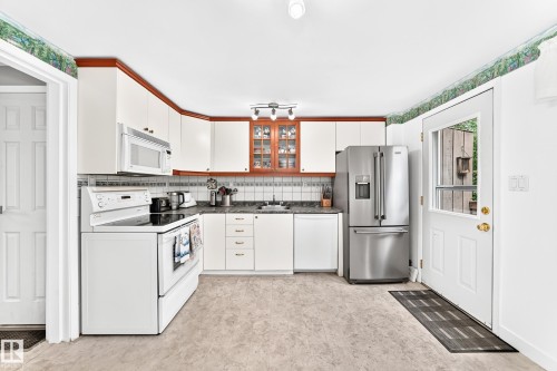 Bright kitchen with white cabinetry, stainless steel refrigerator, white range, and a tiled backsplash - 191 Ridgewood Terrace, St. Albert, AB 