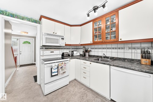 White kitchen cabinetry with wood-finish trim, dark countertops, and a white tile backsplash - 191 Ridgewood Terrace, St. Albert, AB 