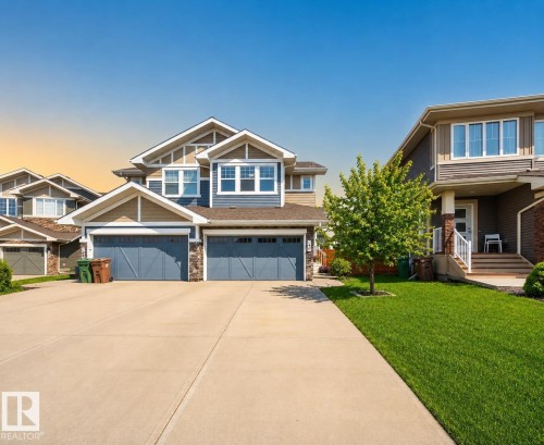 Contemporary multi-story residence featuring a two-car garage, concrete driveway, and a manicured lawn with mature plantings - 70 James Crescent, St. Albert, AB 