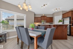 Dining area featuring wood-finish flooring, a contemporary chandelier, and a large window with white blinds - 