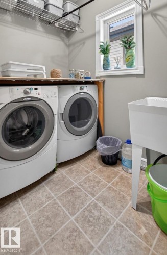 Dedicated laundry area featuring a front-loading washer and dryer, utility sink, window, wire shelving, and wood-finish countertop - 547 Leger Way, Edmonton, AB 