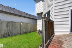 Rear exterior featuring white horizontal siding, a wooden deck with railing, and a vibrant green lawn - 