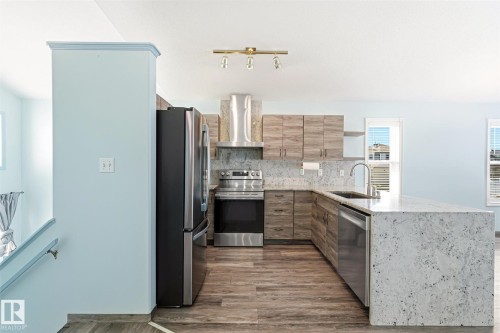 Modern kitchen with light wood-finish cabinetry, stainless steel appliances, and a large central island featuring a light-toned stone countertop - 14908 137 Street, Edmonton, AB 