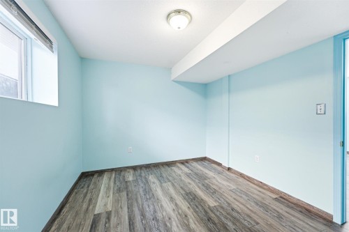 Room featuring light blue painted walls, wood-finish flooring, a window with blinds, and a flush mount ceiling light - 14908 137 Street, Edmonton, AB 