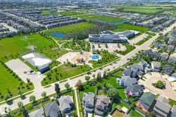 Aerial view of a residential community featuring extensive green spaces, a large recreational park with playground equipment, a modern institutional building, and a distinct sports court - 