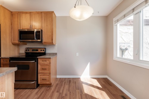 Kitchen and dining area featuring wood-finish flooring, light wood cabinetry, stainless steel appliances, and a white subway tile backsplash - 16B Callingwood Court, Edmonton, AB 