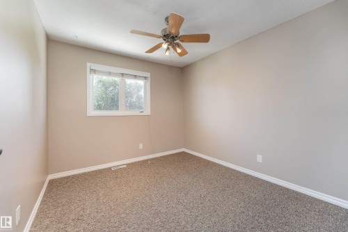 Neutral-toned room featuring a single window, a ceiling fan with light fixture, light gray walls, and carpet flooring - 16B Callingwood Court, Edmonton, AB 