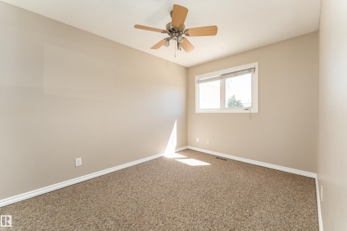 Neutral-toned room featuring a ceiling fan with light fixture, a window with blinds, and brown textured carpet - 16B Callingwood Court, Edmonton, AB 