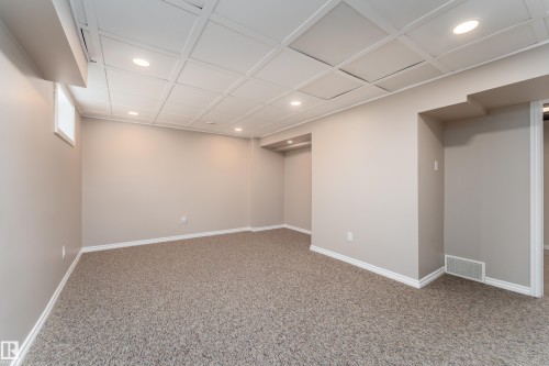 Spacious room featuring textured carpeting, neutral wall paint, and white trim - 16B Callingwood Court, Edmonton, AB 