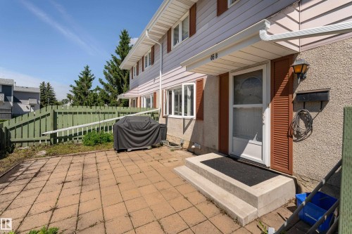 Front exterior featuring a white entry door with an overhead awning, stucco siding, and decorative louvered shutters - 16B Callingwood Court, Edmonton, AB 