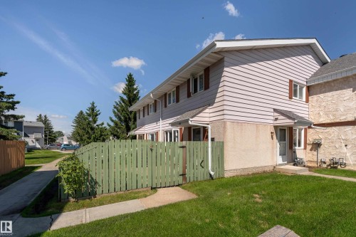 Townhouse exterior featuring horizontal siding, a gabled roofline, and a private fenced yard with mature trees - 16B Callingwood Court, Edmonton, AB 