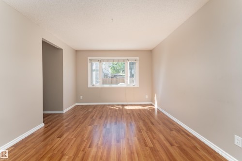 Bright interior space featuring wood-finish flooring, a large window, and light neutral wall tones - 16B Callingwood Court, Edmonton, AB 