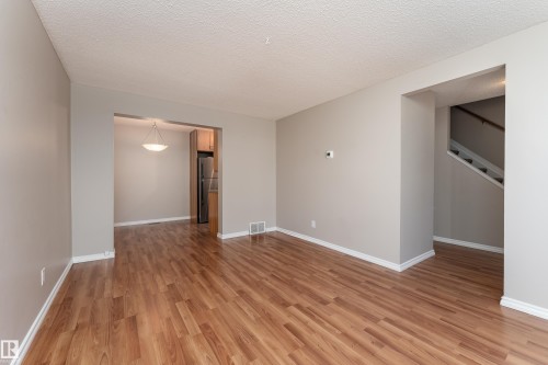 Spacious room featuring wood-finish flooring, light gray walls, white baseboards, and a textured white ceiling - 16B Callingwood Court, Edmonton, AB 