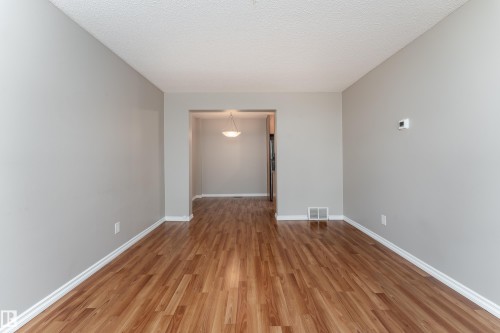 Spacious room featuring wood-finish flooring, light gray walls, white baseboards, and a textured ceiling - 16B Callingwood Court, Edmonton, AB 